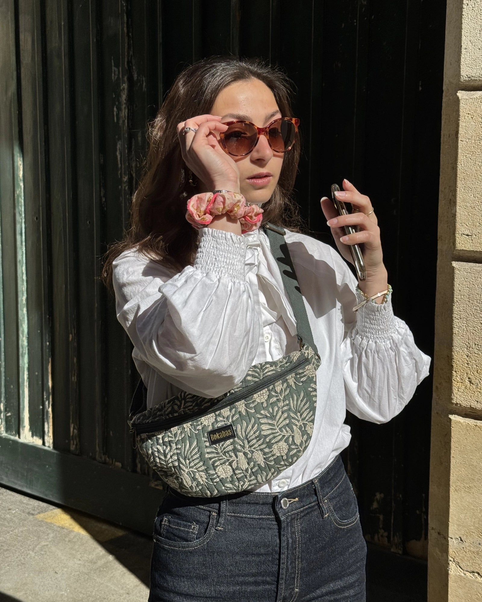 Sac banane matelassé Bokabas, imprimé Dema vert sauge, porté en bandoulière sur chemise blanche