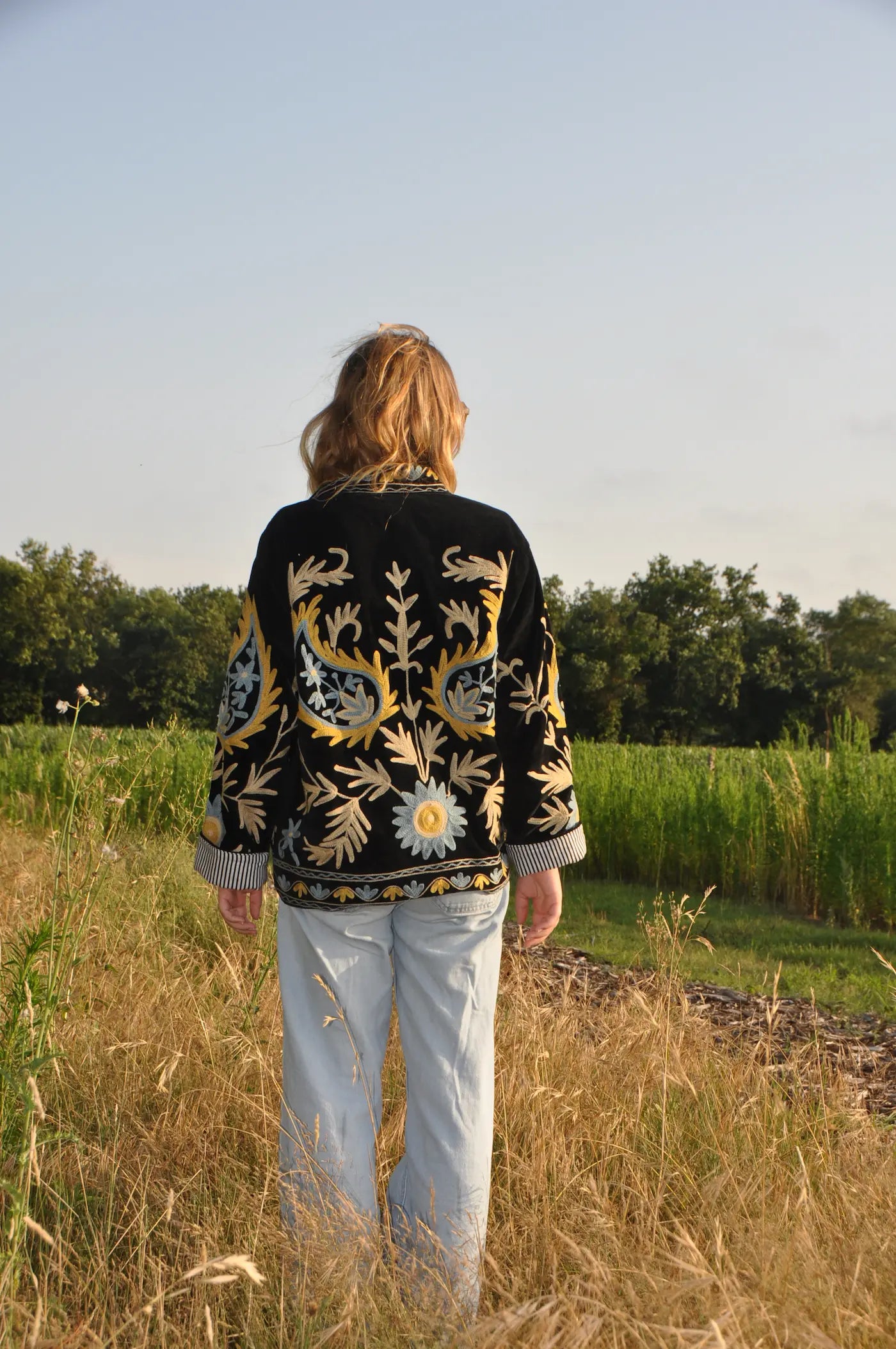 Veste noire brodée fleurie portée de dos en marchant dans un paysage naturel – Bokabas